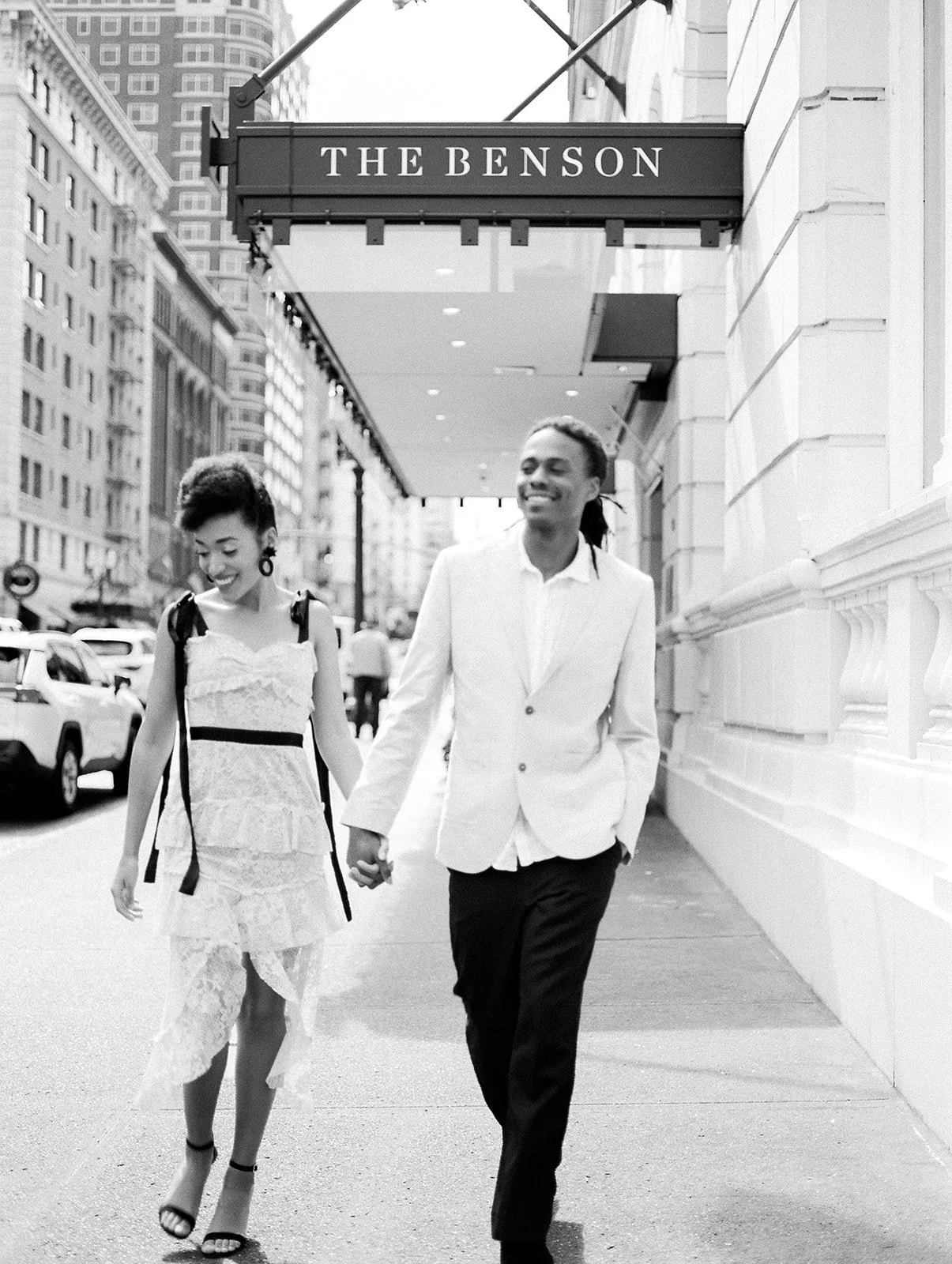 Black and white photo of couple walking under The Benson Hotel sign in Portland