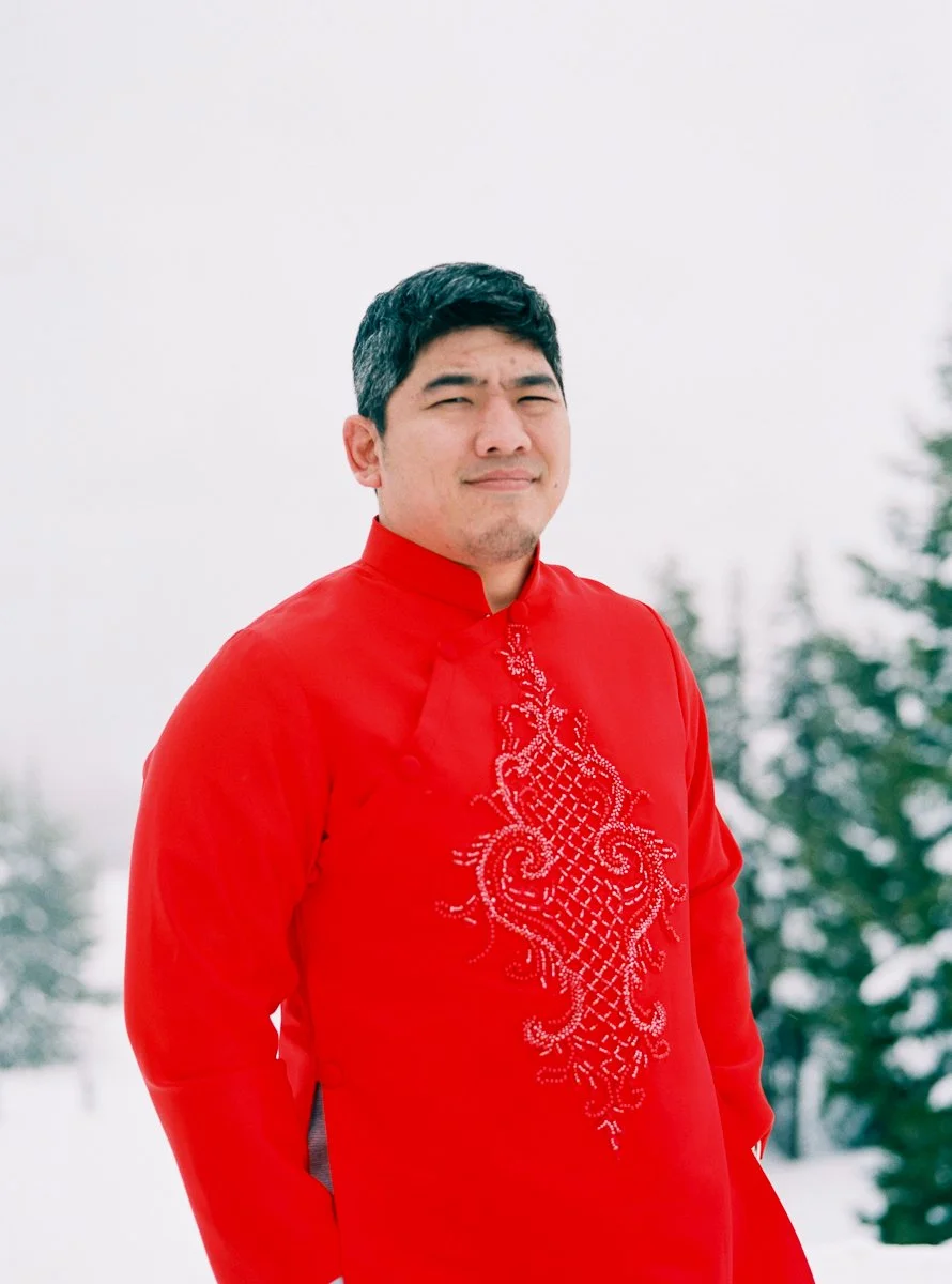 Portrait of groom in red embroidered Vietnamese áo dài in snowy Mount Hood setting.