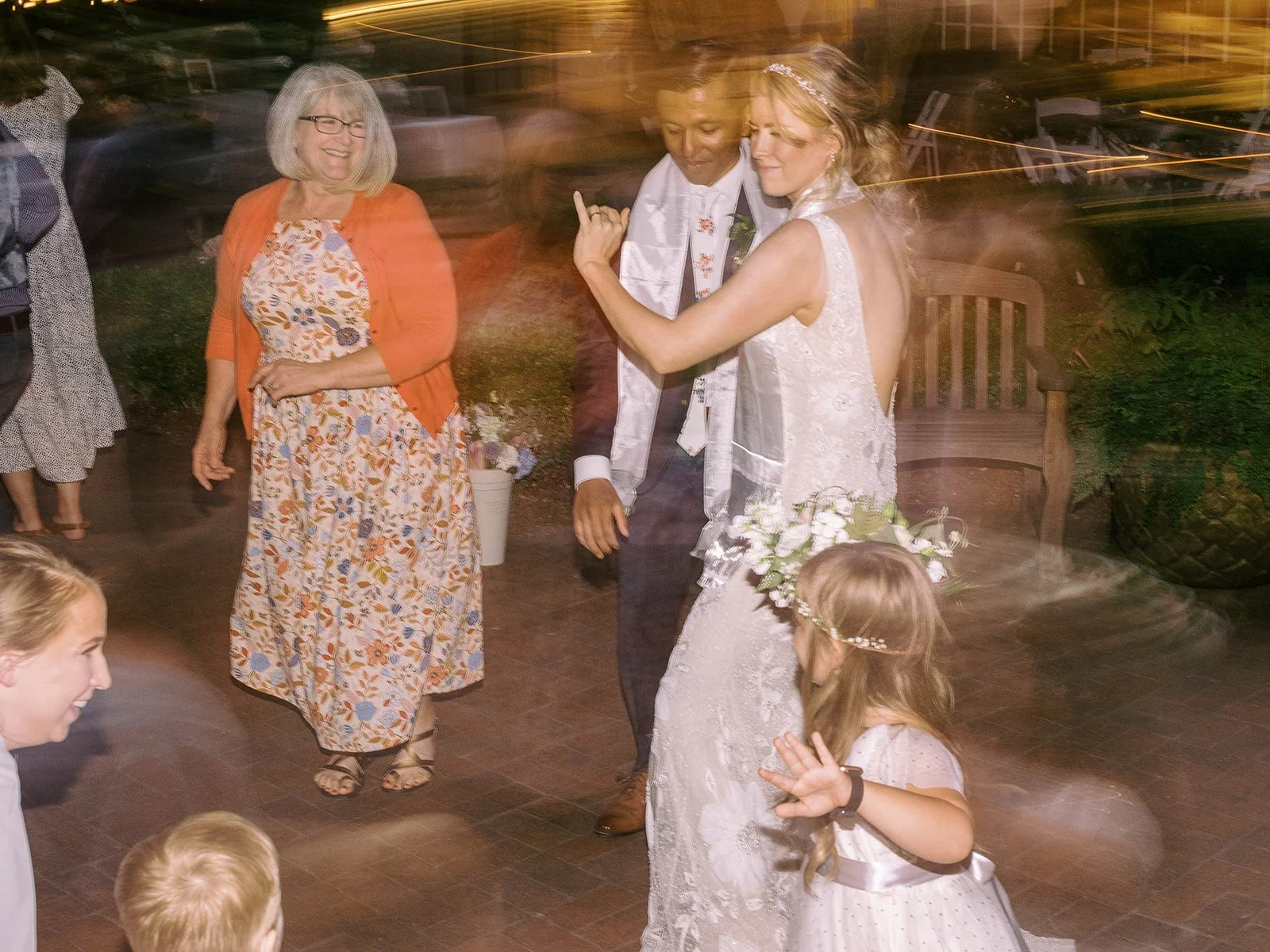 Bride and groom dance with guests during the evening reception in the garden.