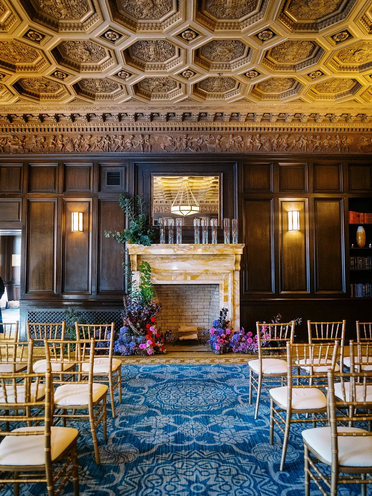 Historic wedding ceremony room with dark wood, blue patterned carpet and colorful floral arrangements