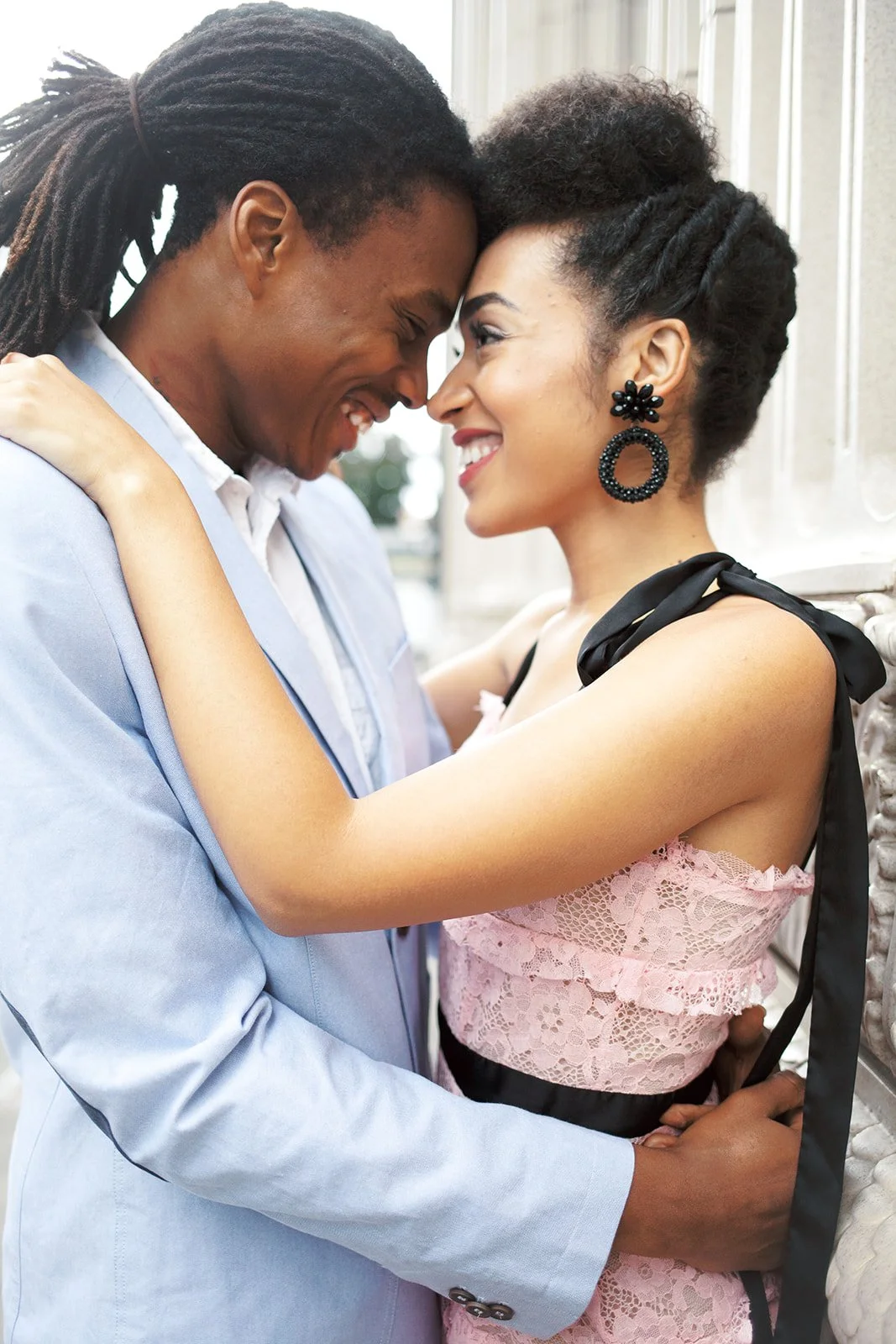 Intimate portrait of couple with foreheads touching, standing against textured Portland wall