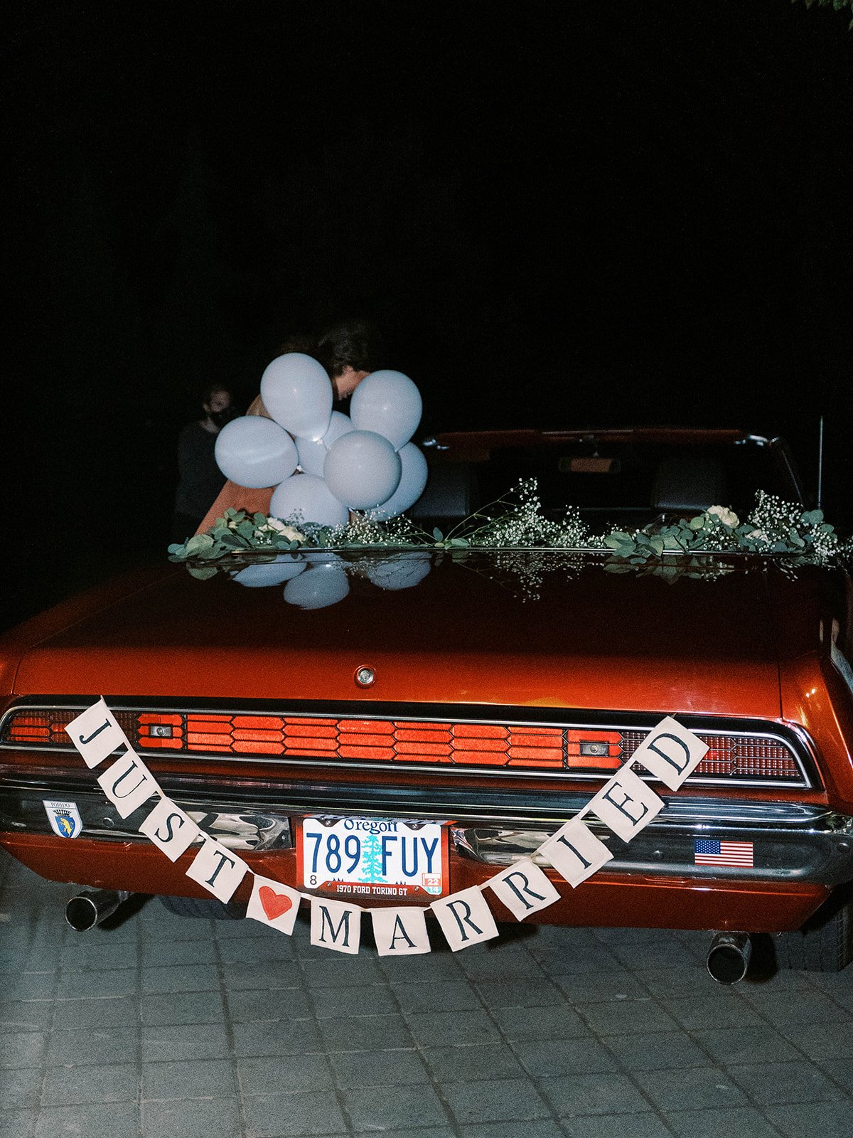 Vintage red getaway car decorated with greenery, white flowers, balloons and a “Just Married” banner.