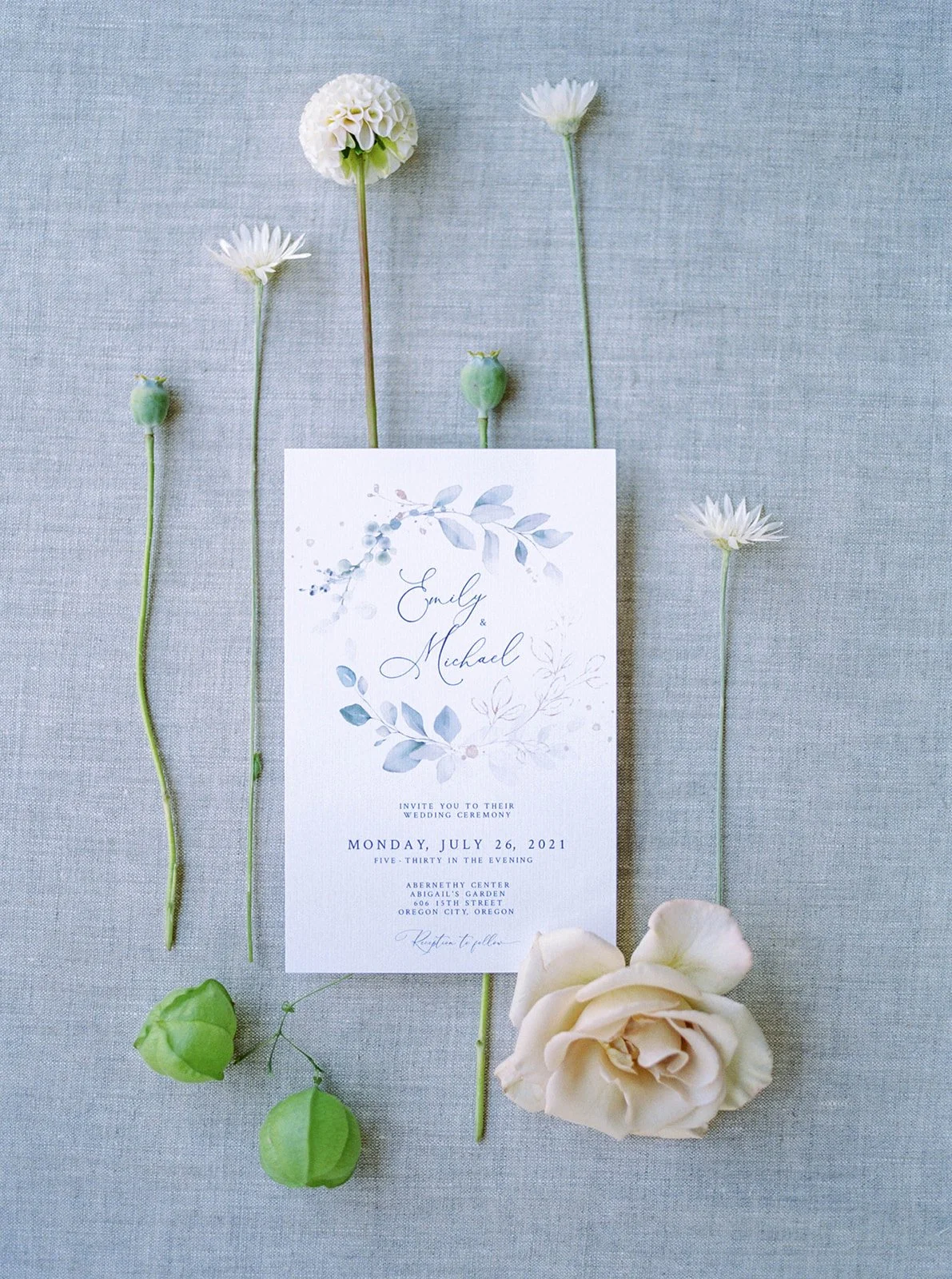 Blue watercolor wedding invitation suite styled with delicate white blooms and garden-inspired details.