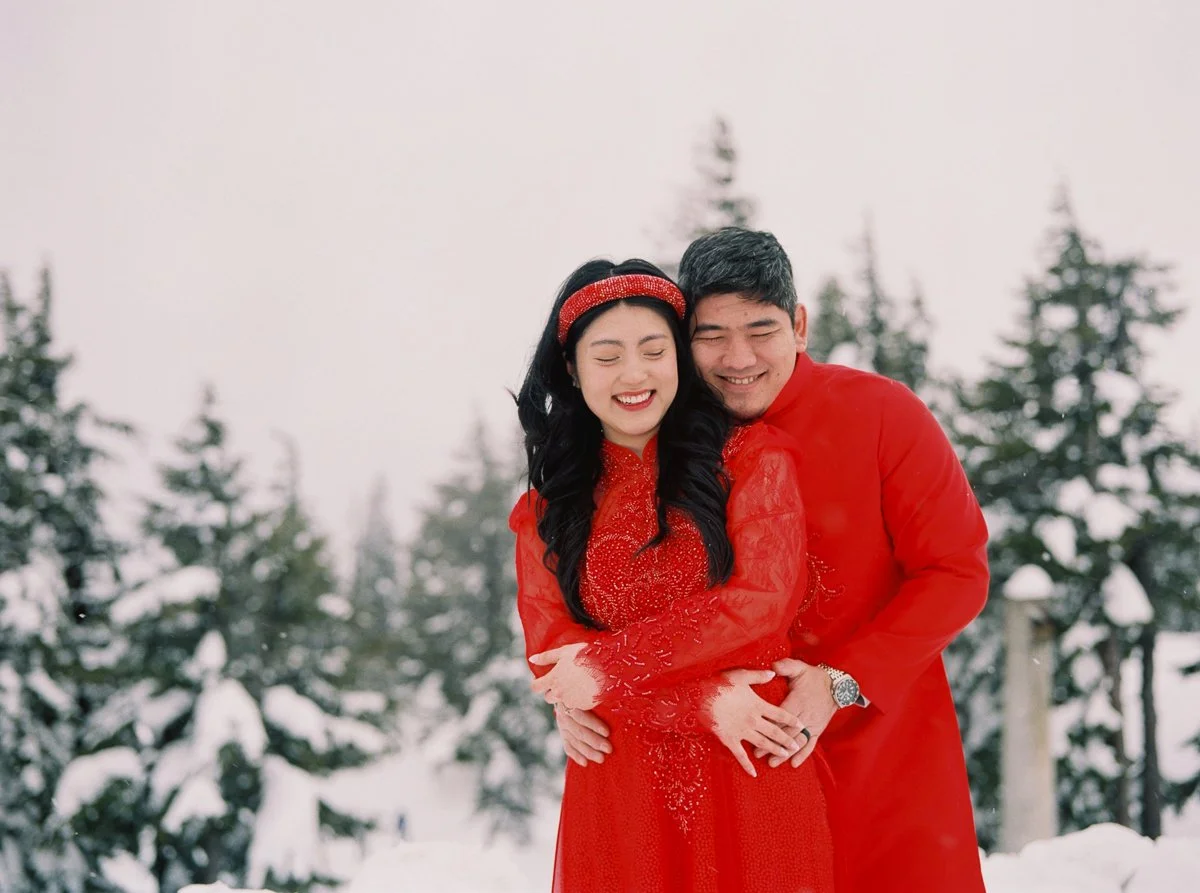 Couple smiling as the groom embraces the bride from behind in snowy Mount Hood landscape.