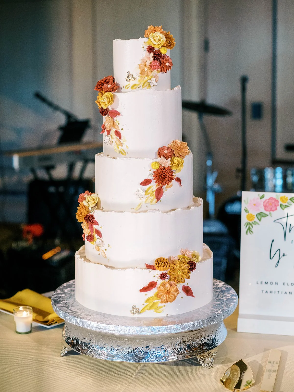 Full view of the four-tier white wedding cake with cascading sugar flowers in rust, yellow, and peach tones on a silver cake stand
Bride and groom sharing their first dance on the ballroom floor while a live band performs behind them
Playful cake cut