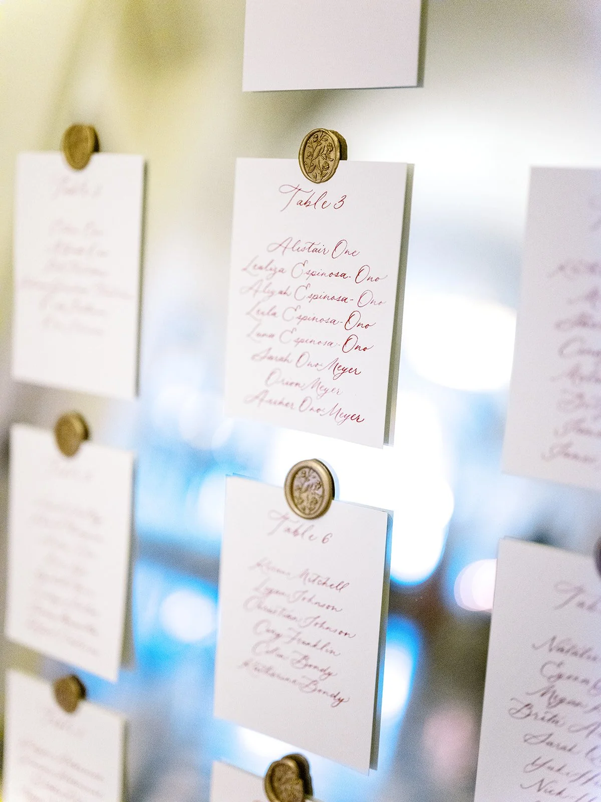 Minimalist seating chart cards with handwritten names clipped to a display board with gold pins and soft lighting.
