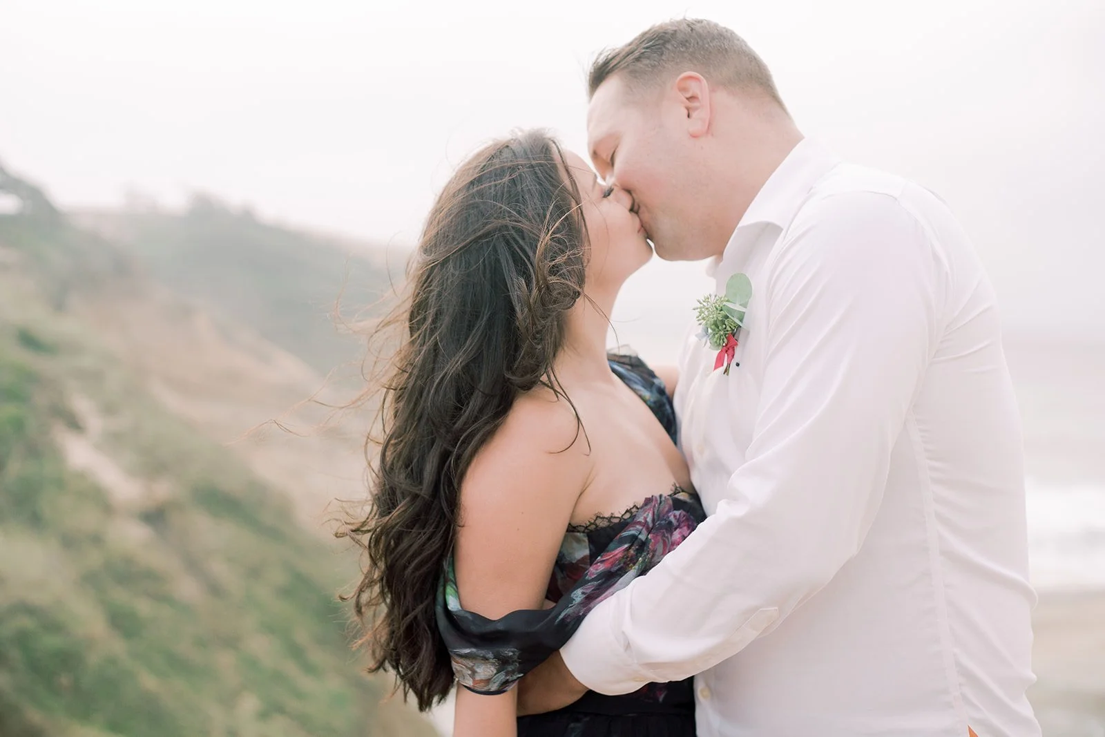 Close-up of couple kissing on Oregon Coast cliffs, wind blowing through hair, soft neutral tones