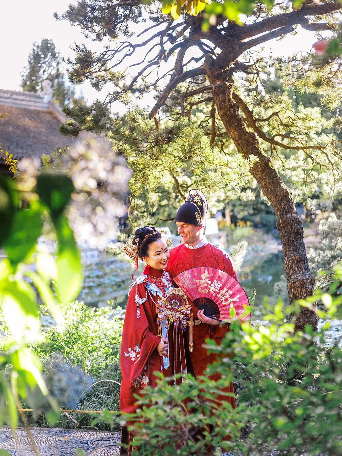 Bride and groom sharing a tender moment beside the koi pond at Lan Su, surrounded by pine trees in warm afternoon light