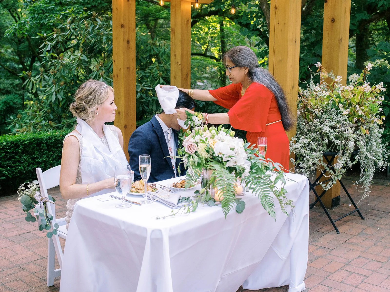 Groom’s mother places a ceremonial cloth over him during a cultural wedding blessing.