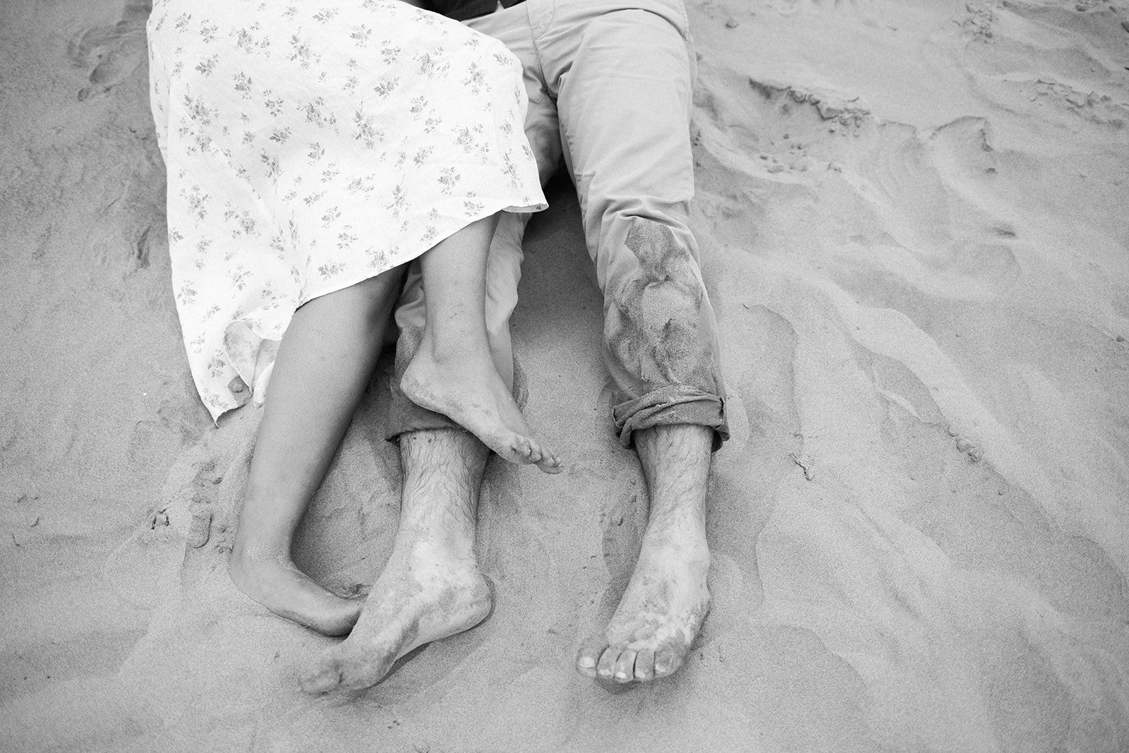 Close-up of couple’s sandy feet intertwined on beach, black and white detail shot