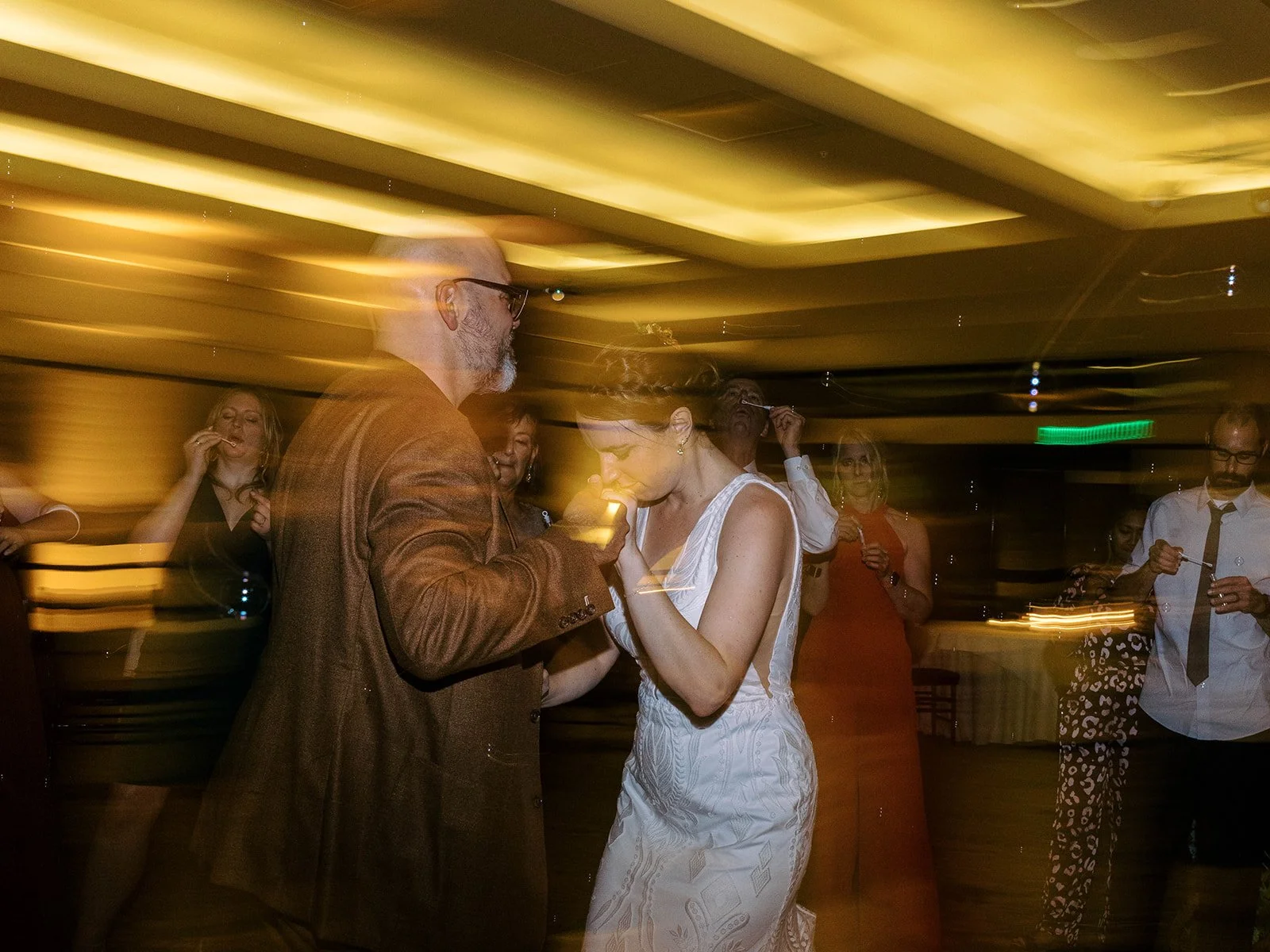 Bride and groom in  dance moment with dramatic warm motion blur and bubble-blowing guests surrounding them