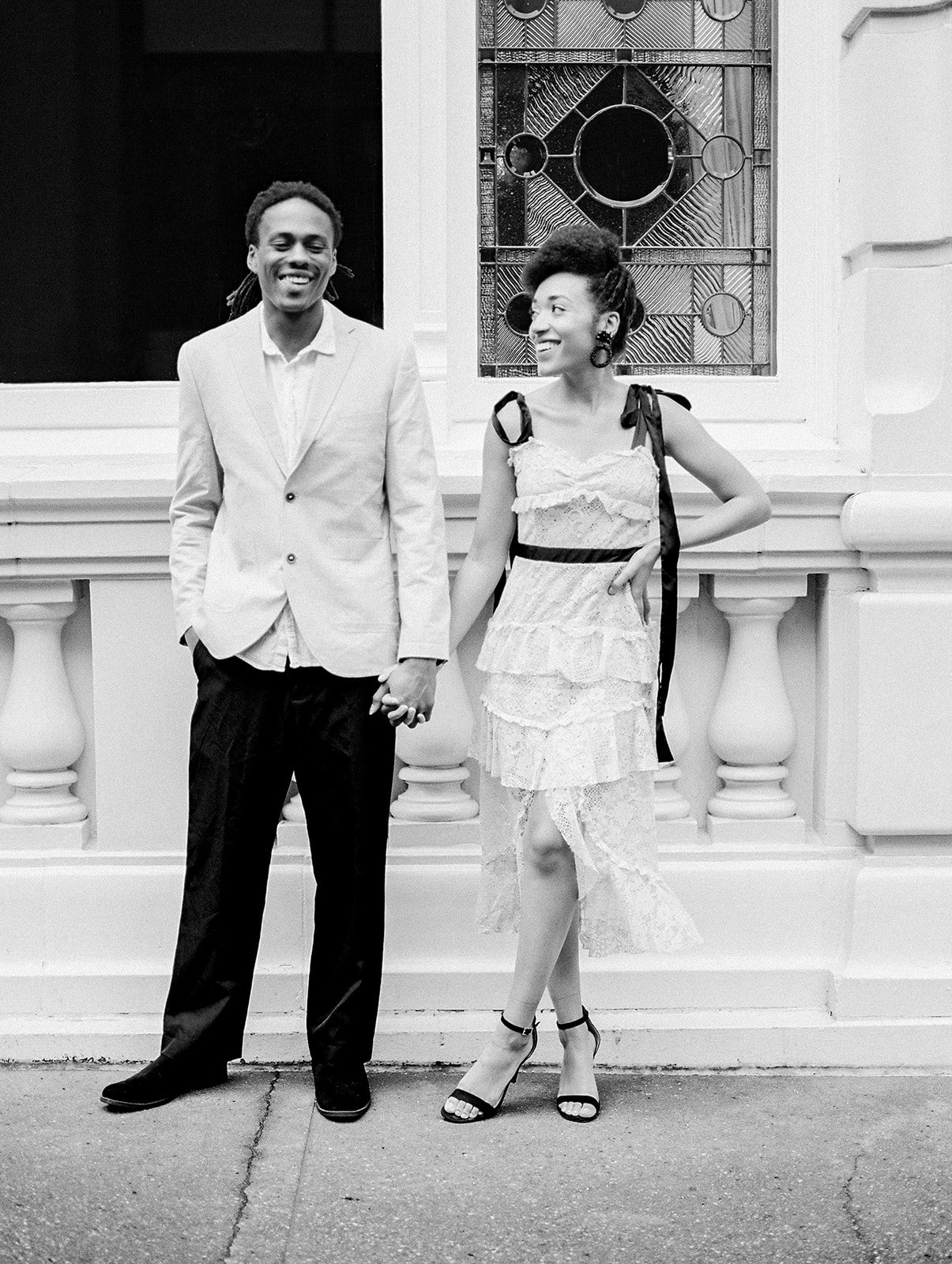 Couple holding hands and smiling in front of decorative Portland building with stained glass window