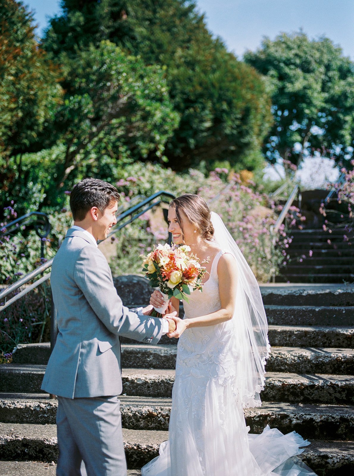 Bride and groom holding hands on garden steps, surrounded by blooming flowers at Oregon Gardens.