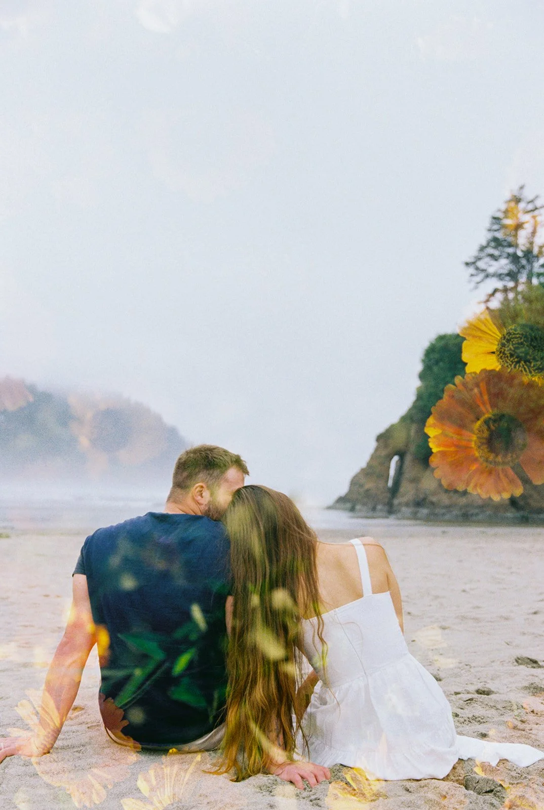 Couple sitting on a sandy beach with cliffs in the background, overlaid with soft floral double exposure.
