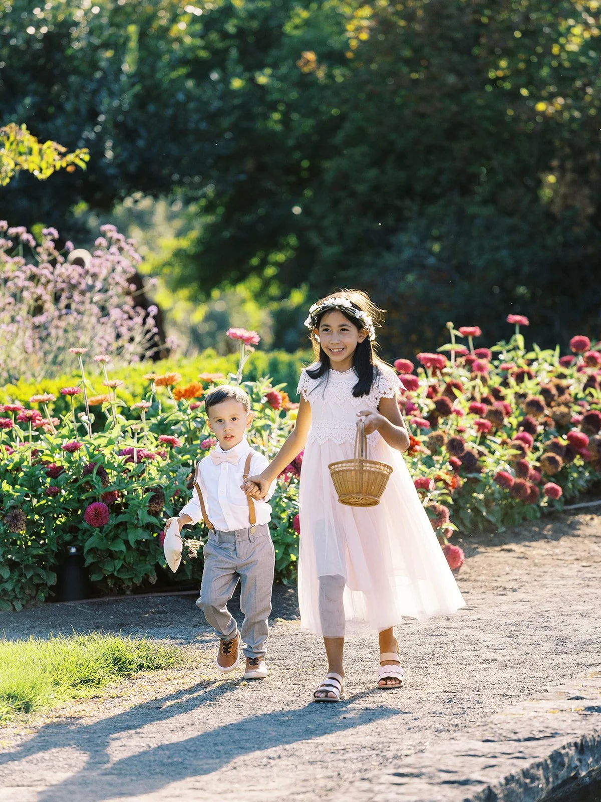 Young flower girl and ring bearer walking through a colorful garden toward the wedding ceremony.