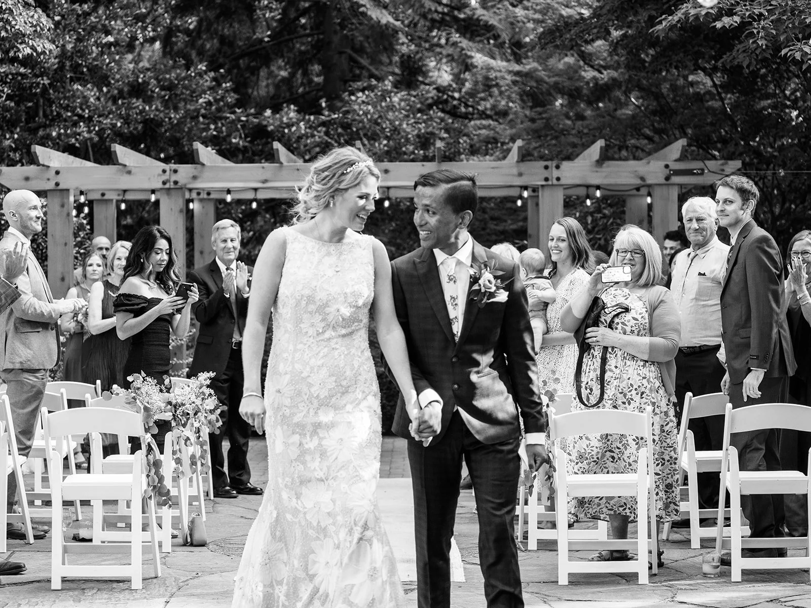Bride and groom walk back down the aisle together as guests applaud around them.