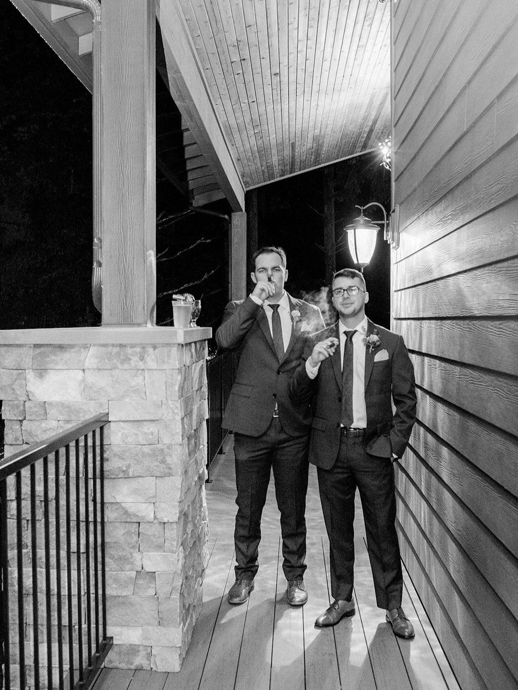 Black-and-white nighttime portrait of two groomsmen standing outside in suits.