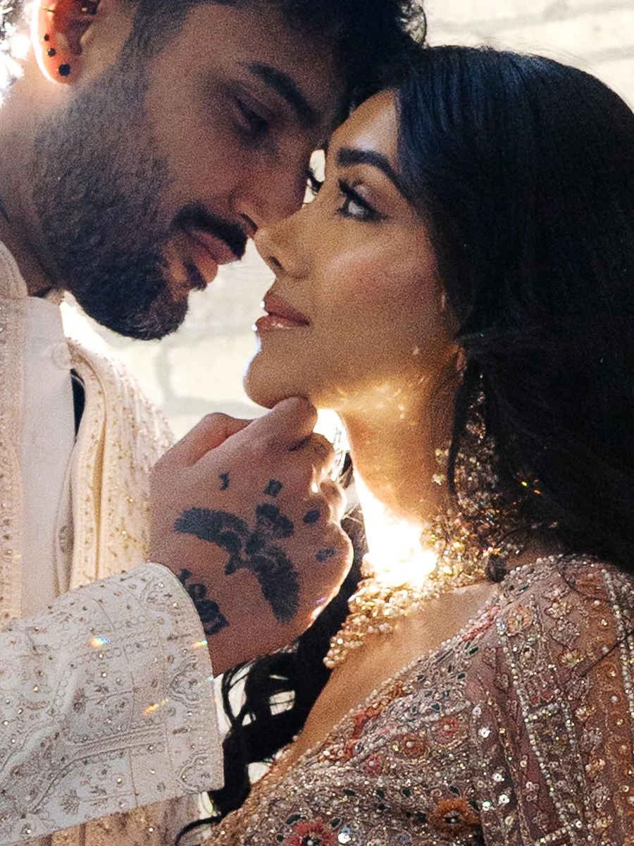 Intimate close-up portrait of South Asian couple in embellished wedding attire with warm sunlight and sparkling jewelry details.