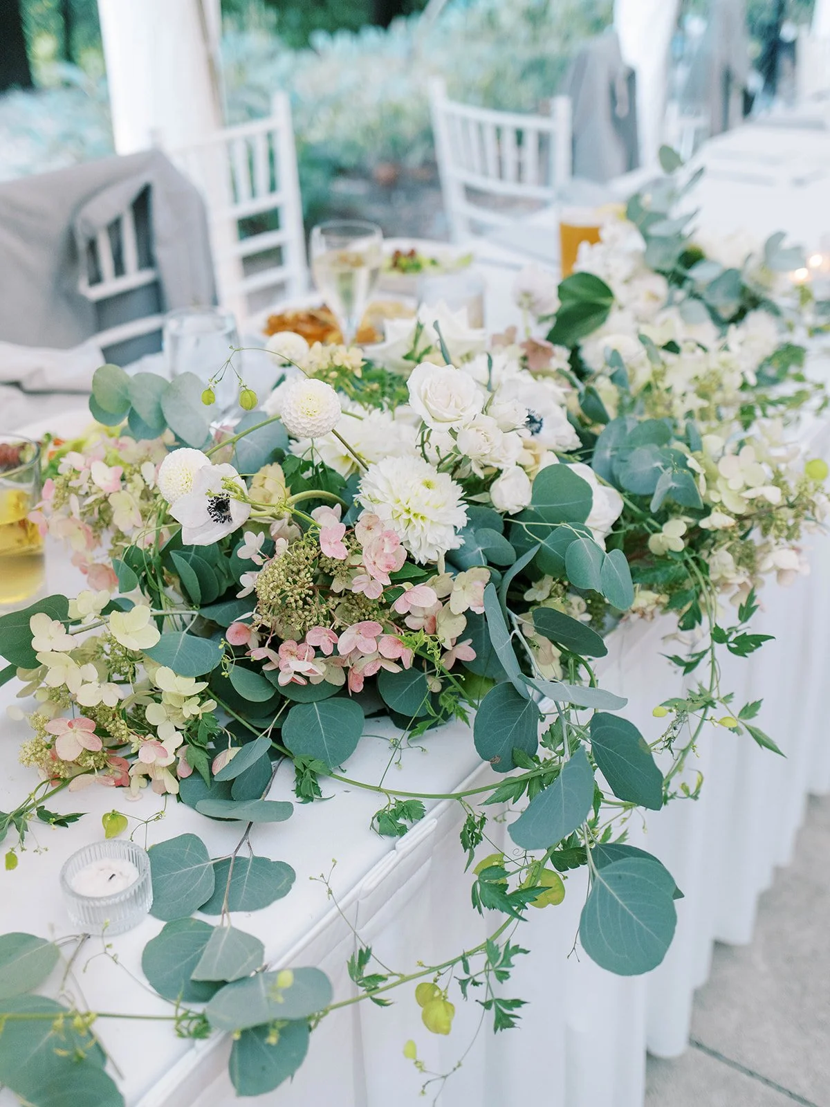 Long floral arrangement with eucalyptus, white blooms, and blush accents decorating a wedding head table