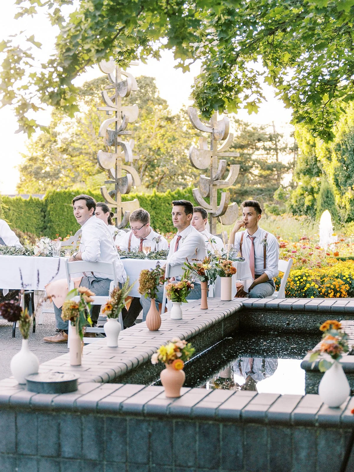 Wedding guests seated at reception tables beside reflecting pool with floral decor