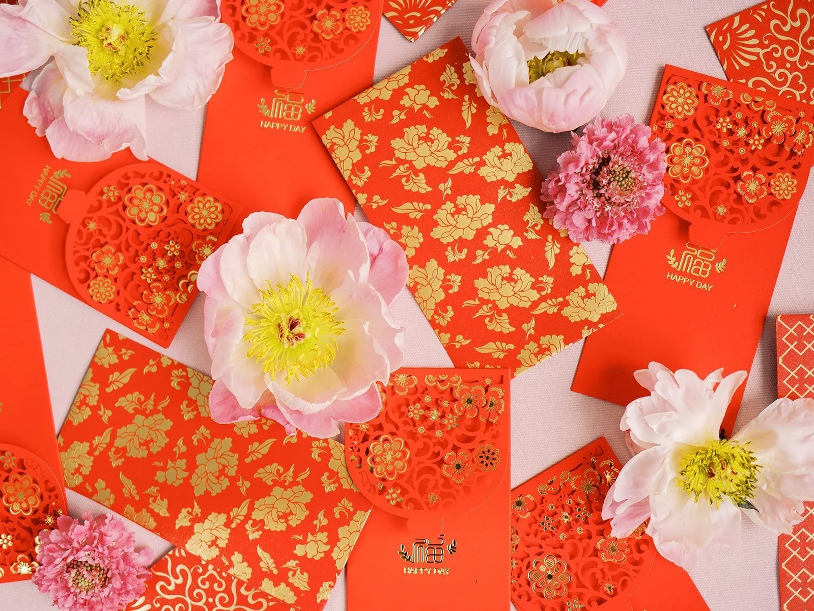 Red and gold Chinese envelopes arranged with pink and white flowers for a wedding celebration
