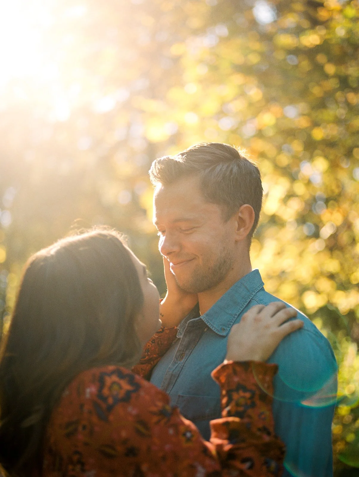 Intimate close-up of couple with warm sunlight and autumn foliage creating a soft glow in forest setting