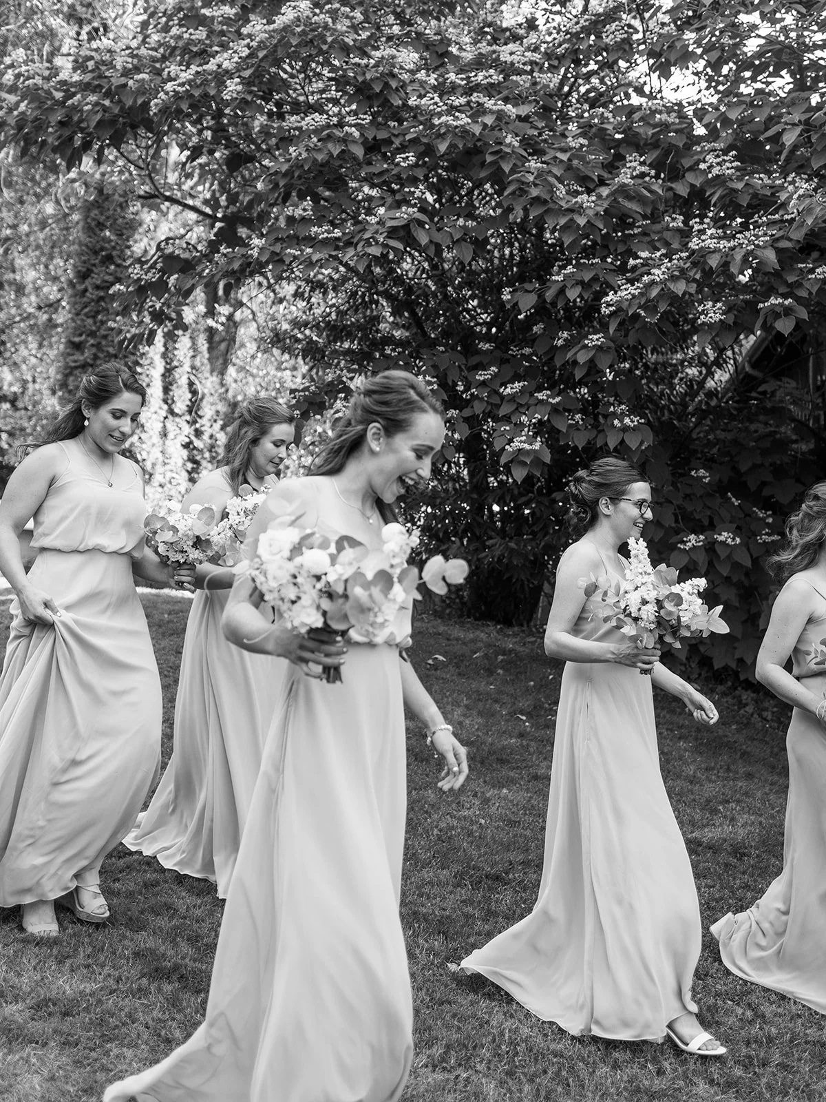 Bride and bridal party walking together across garden lawn at Abernathy Center wedding venue.