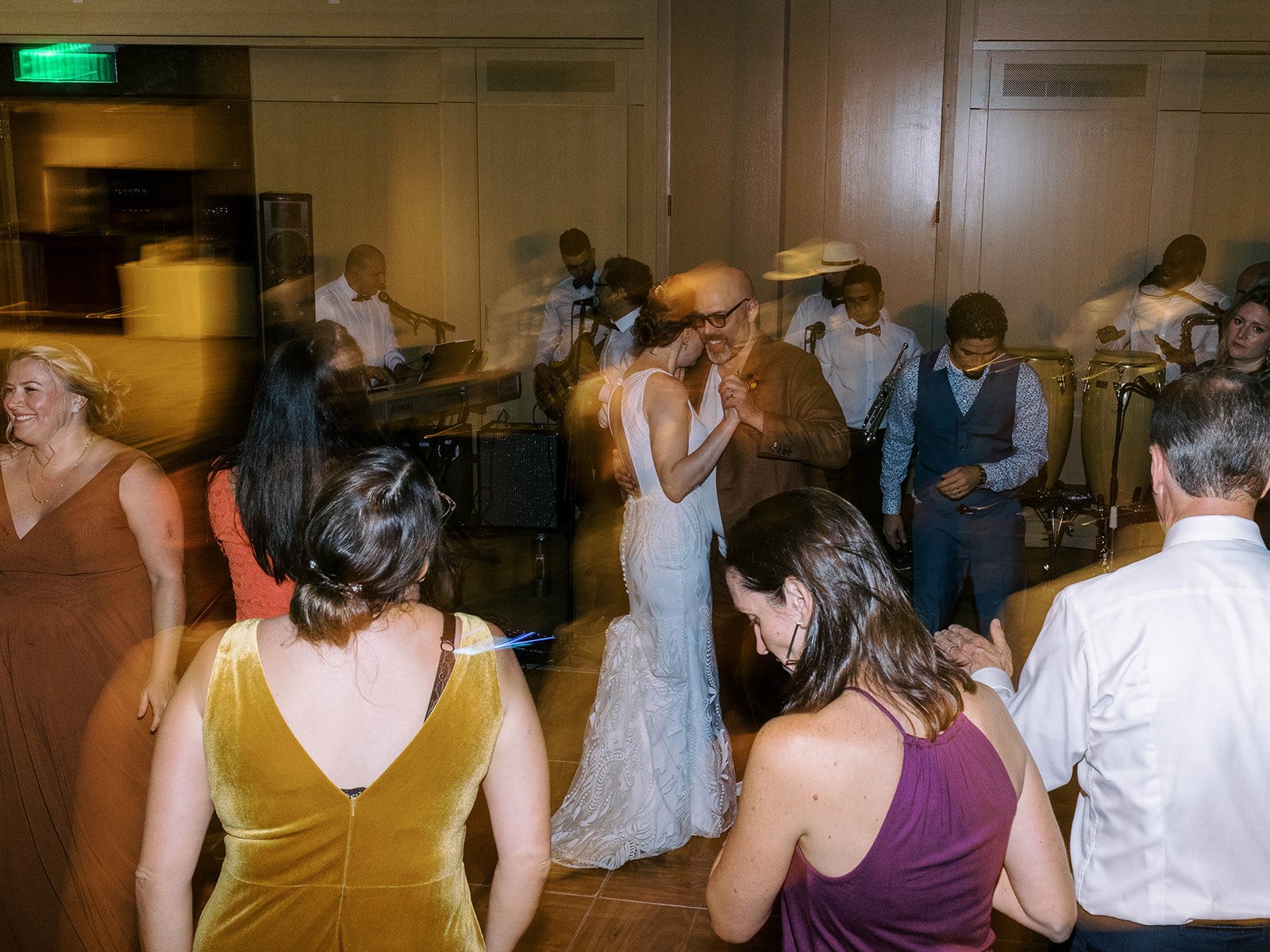 Newlyweds dancing together on the reception floor as guests and a live band surround them.