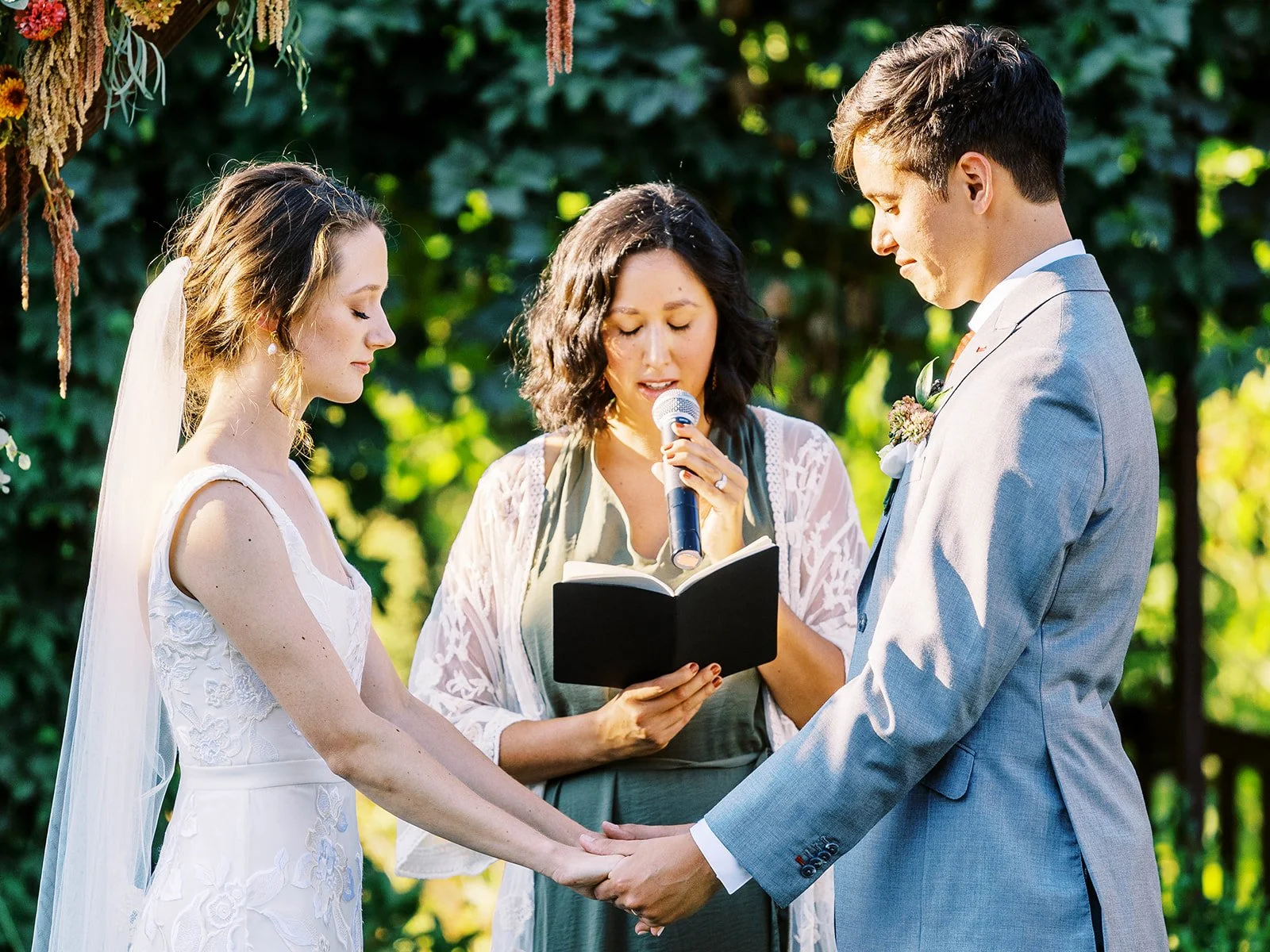 Bride and groom holding hands as the officiant reads during their outdoor wedding ceremony.