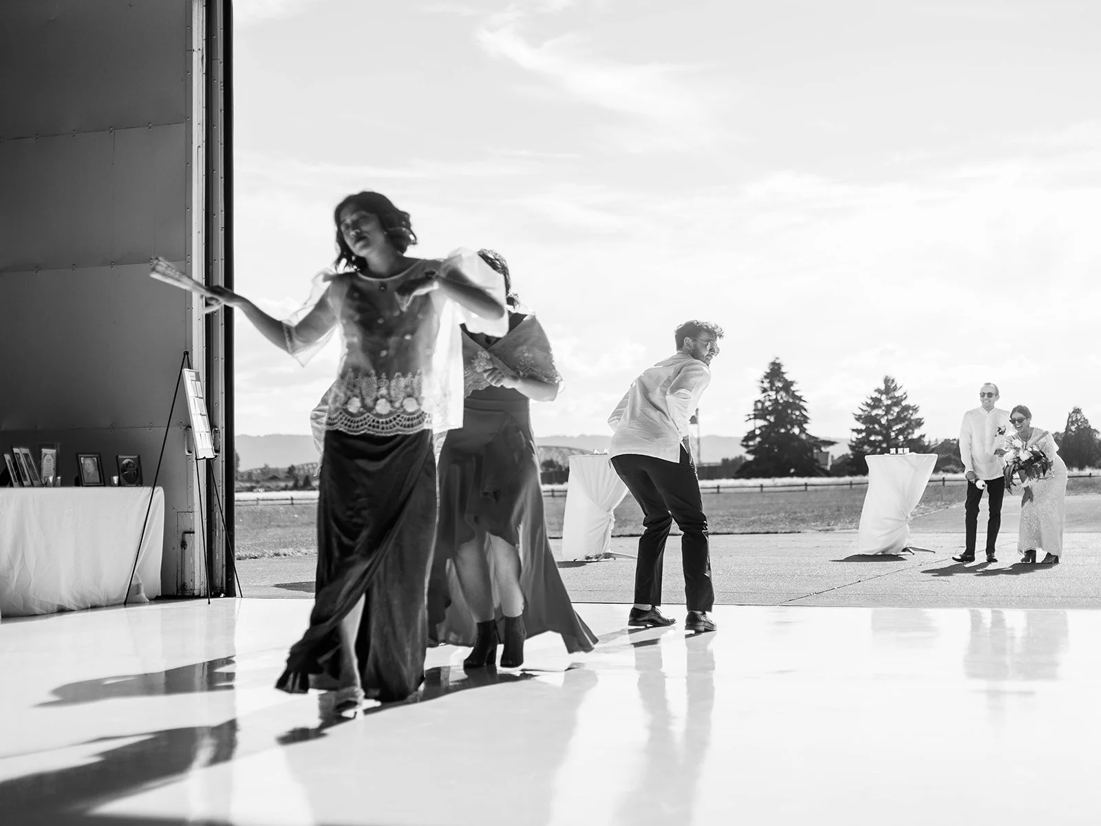 Black and white image of wedding party members dancing energetically during the reception grand entrance as the bride and groom approach in the background
