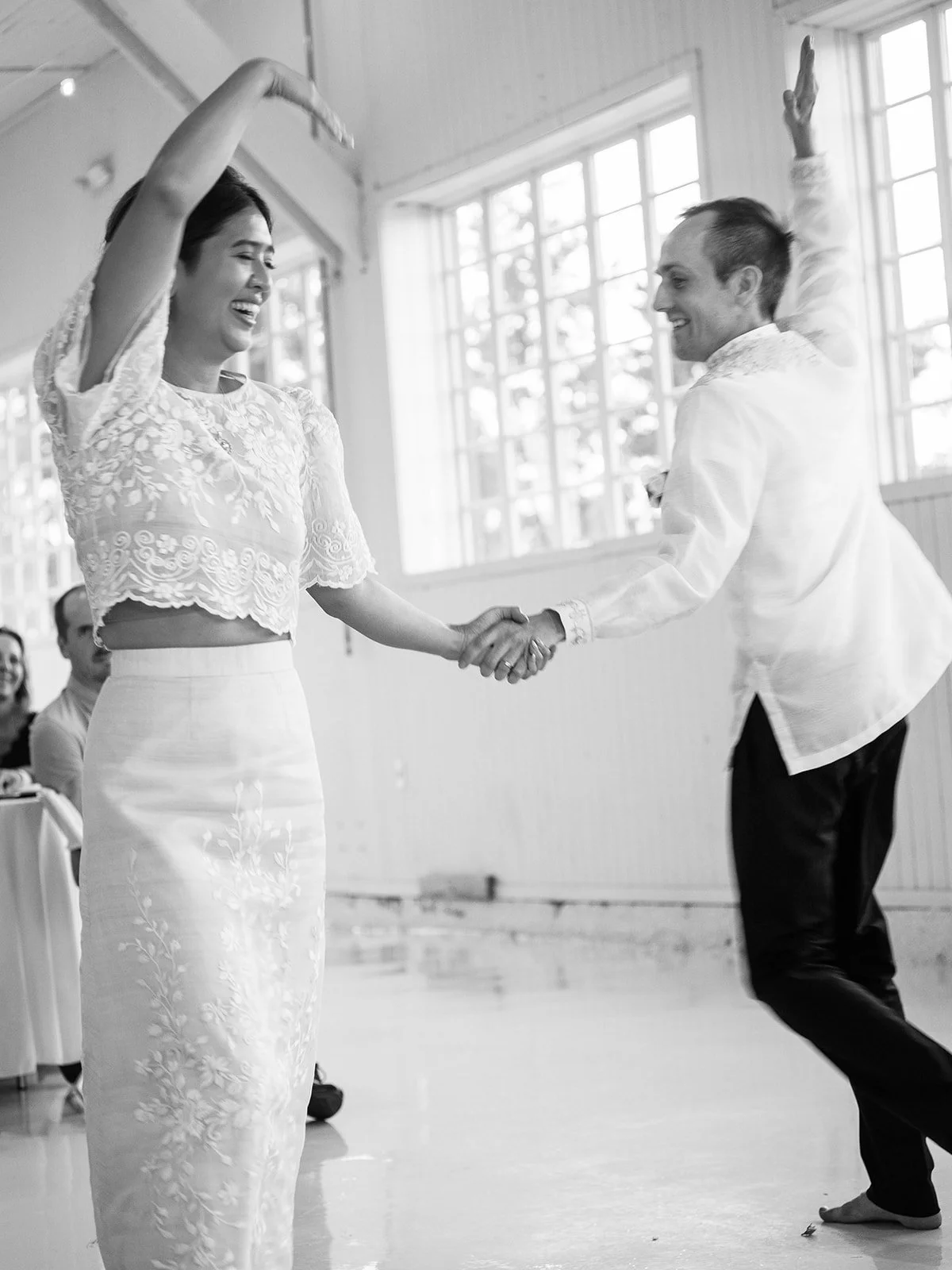Black and white image of the bride and groom dancing with arms raised joyfully during their first dance inside the Pearson Air Museum hangar
