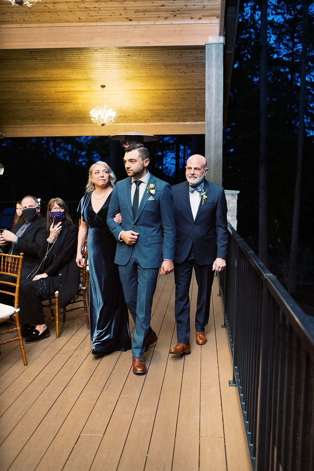 Groom walks down the aisle with two family members at the start of the evening wedding ceremony.