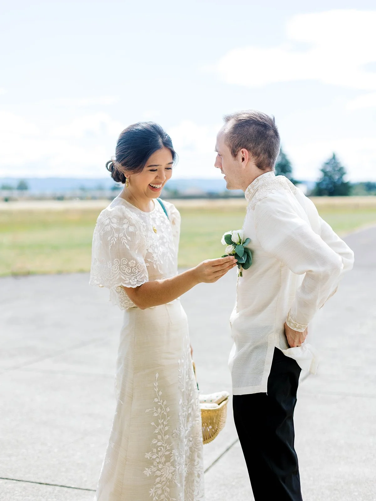 Bride laughing while pinning the groom's boutonniere on the airfield tarmac during their first look
