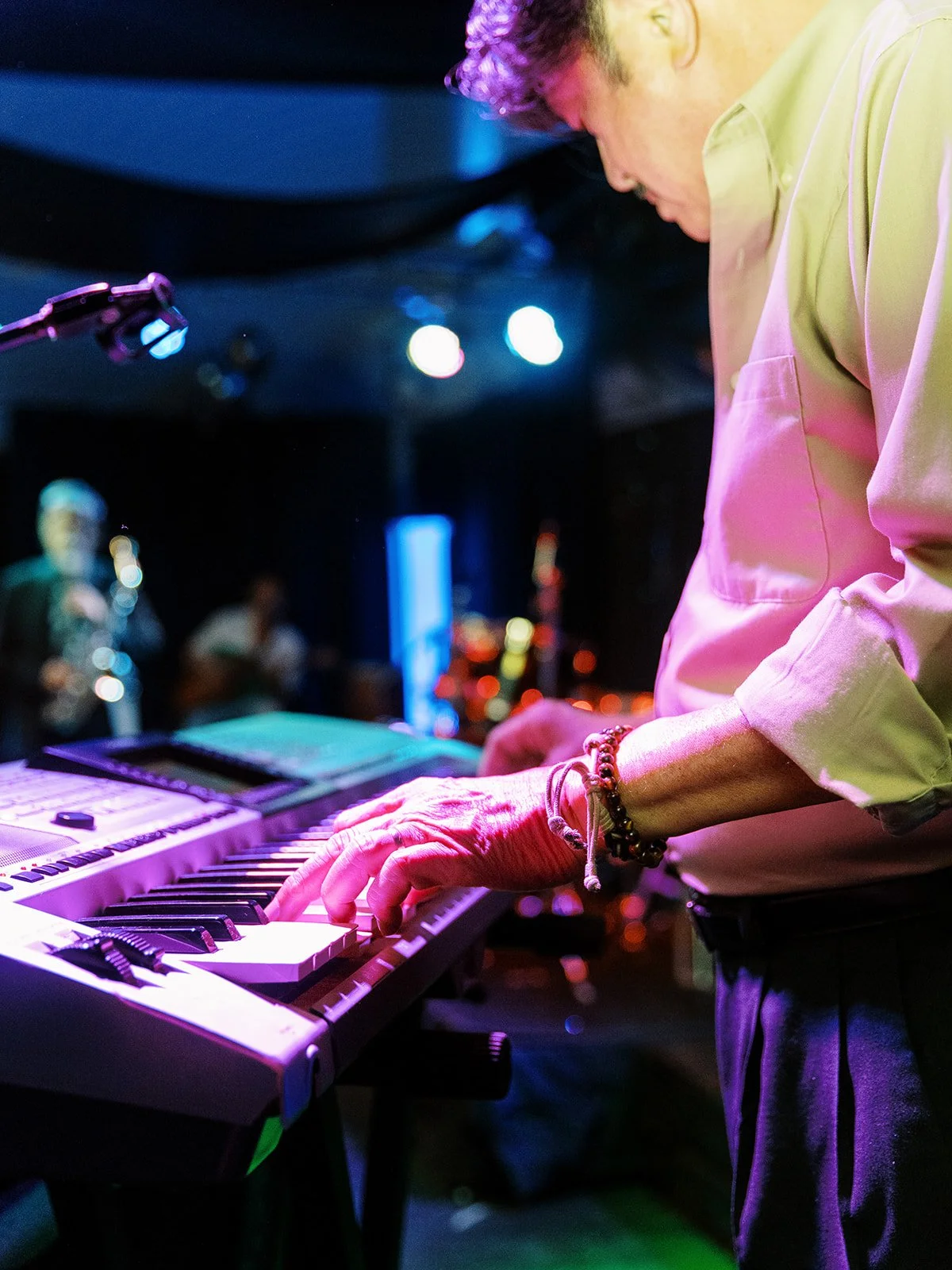 Close-up of a keyboardist's hands playing a Yamaha keyboard on stage at the Mekong Bistro reception, stage lights glowing behind him
