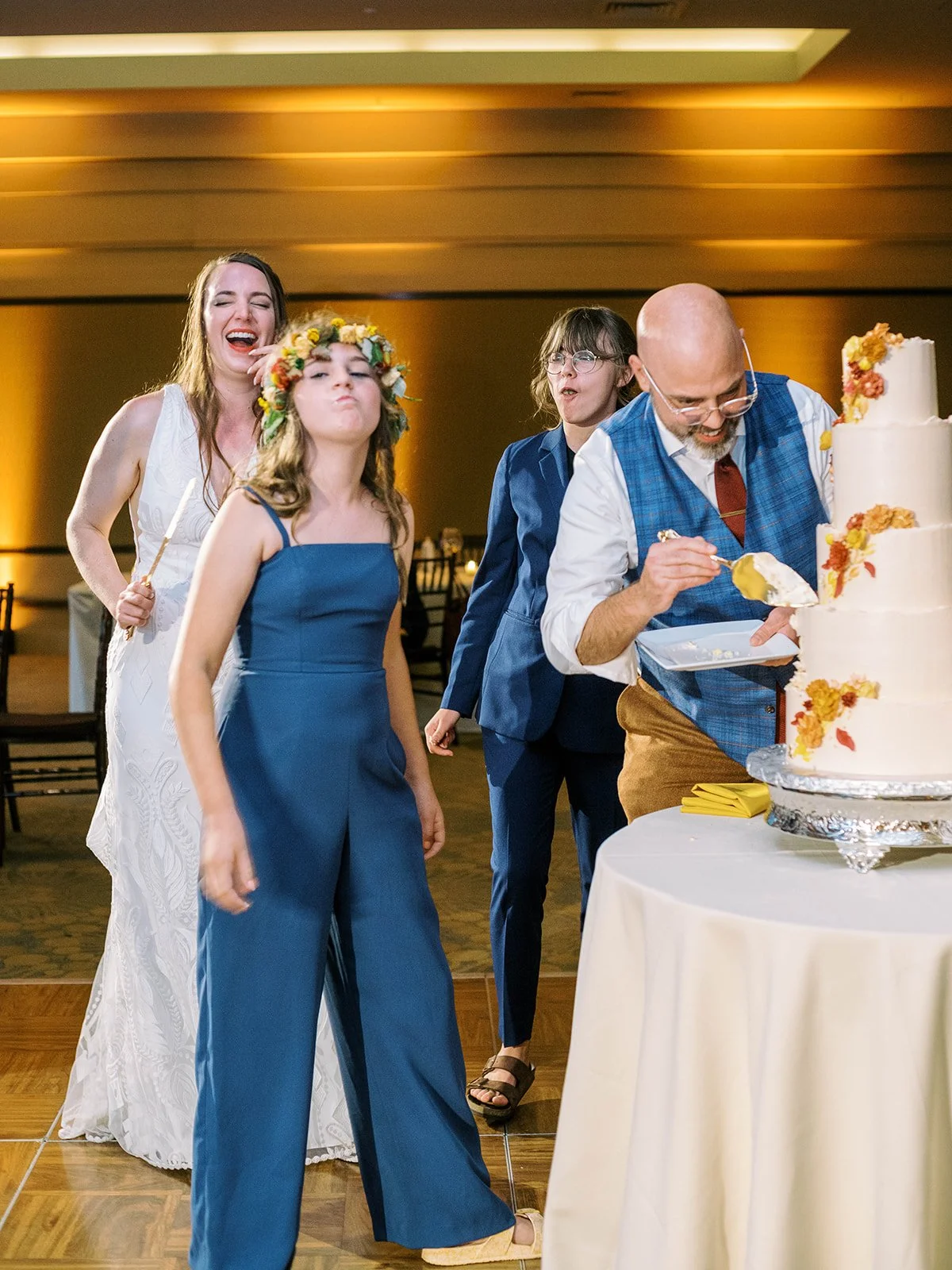 Playful cake cutting moment with the bride laughing and two children making funny faces as the groom scoops a piece