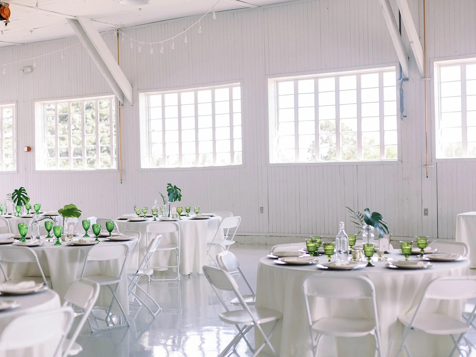 Wide view of the Pearson Air Museum hangar reception space with round tables, white linens, green glassware, and abundant natural light.