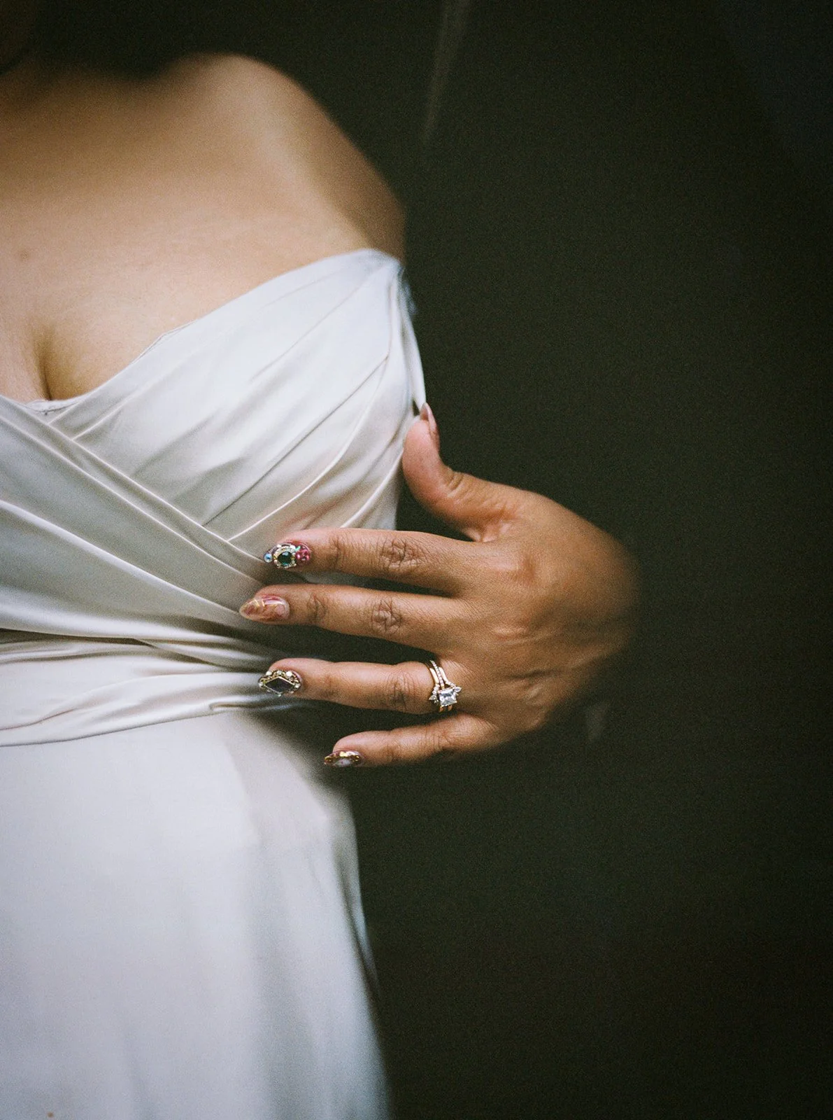 Close-up of bride’s hand with engagement ring resting on draped off-shoulder wedding dress fabric.