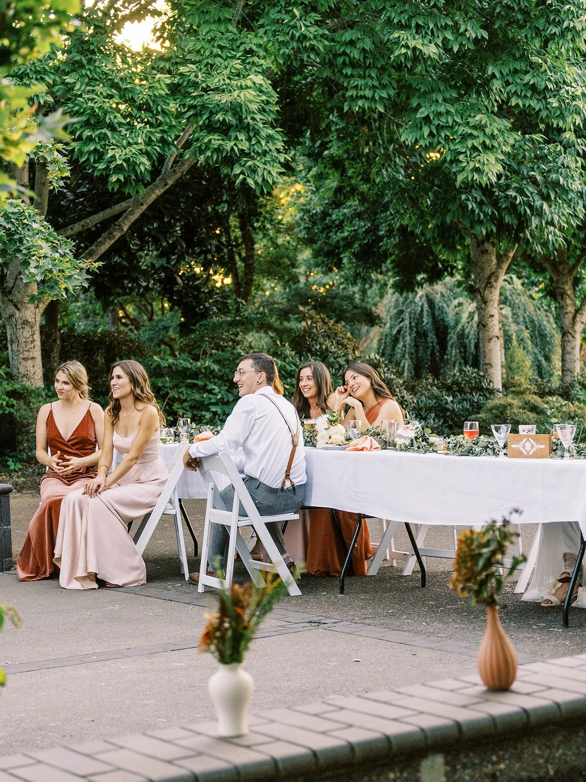 Guests seated at long reception table in garden setting with greenery and soft light