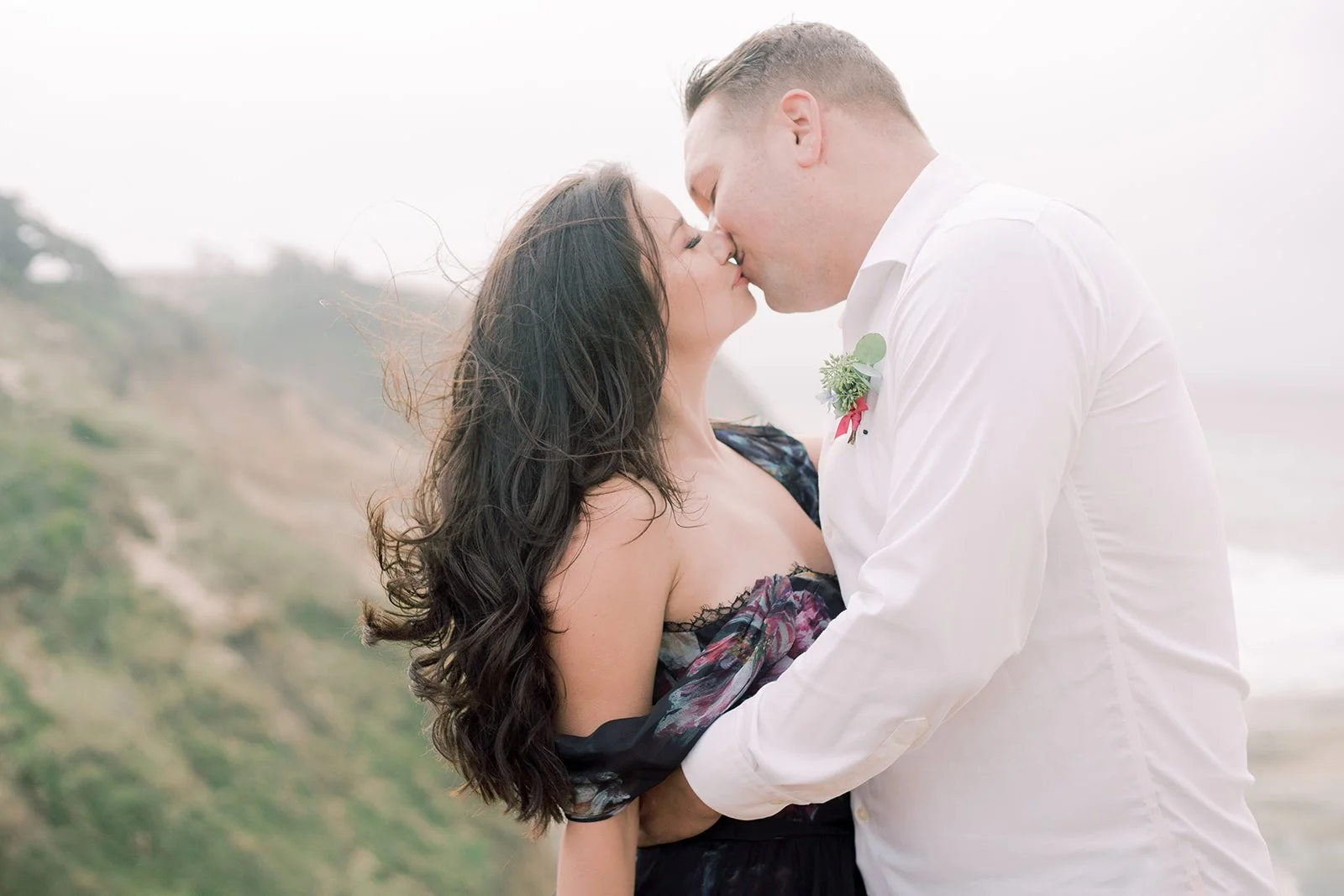 Intimate coastal portrait of couple kissing, ocean cliffs blurred in background, breezy Oregon shoreline