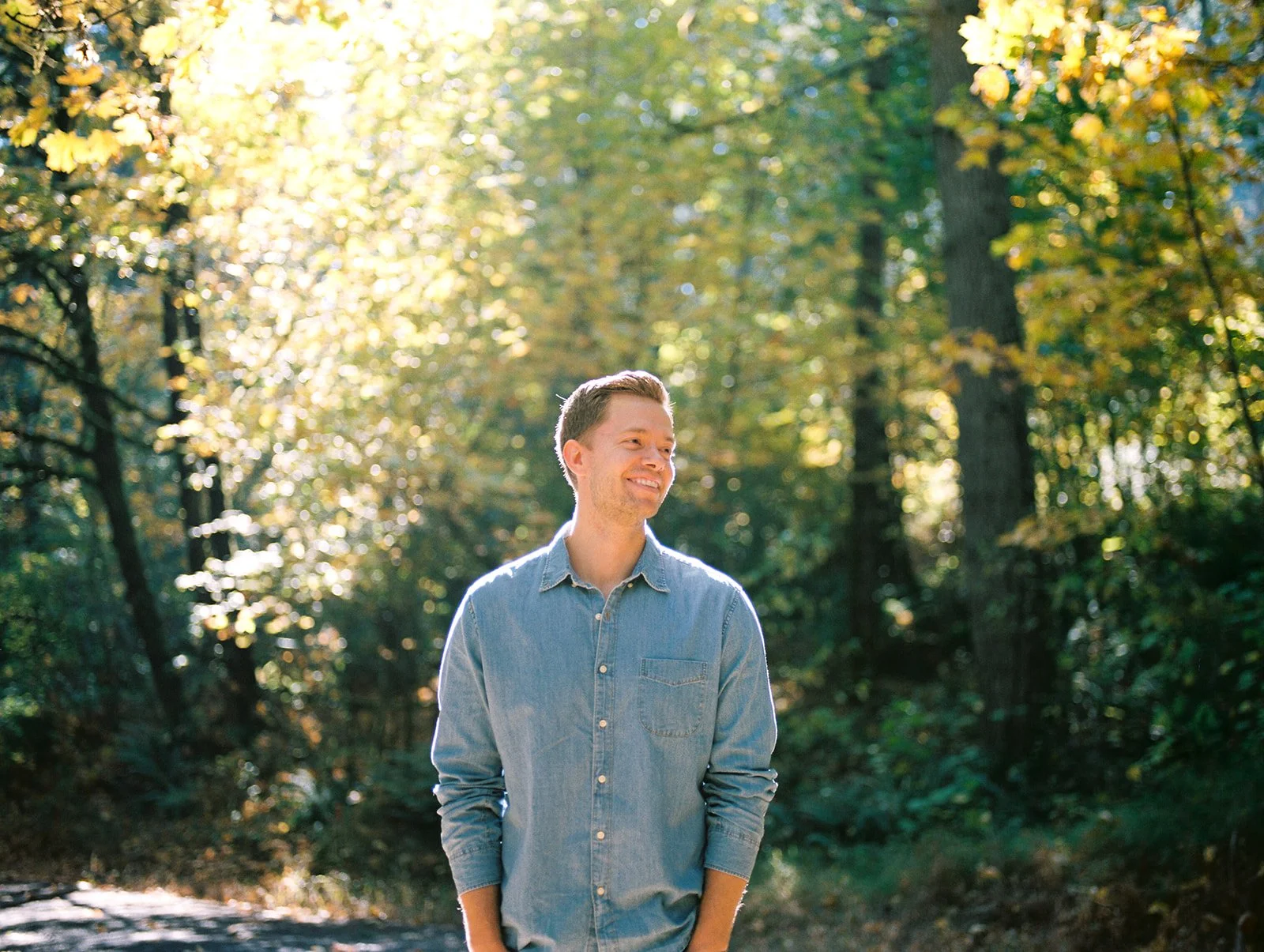 Portrait of man standing on forest path with sunlight filtering through fall trees in Oregon