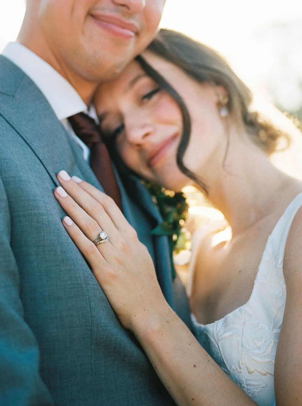 Close-up of bride resting head on groom’s shoulder showing wedding ring detail