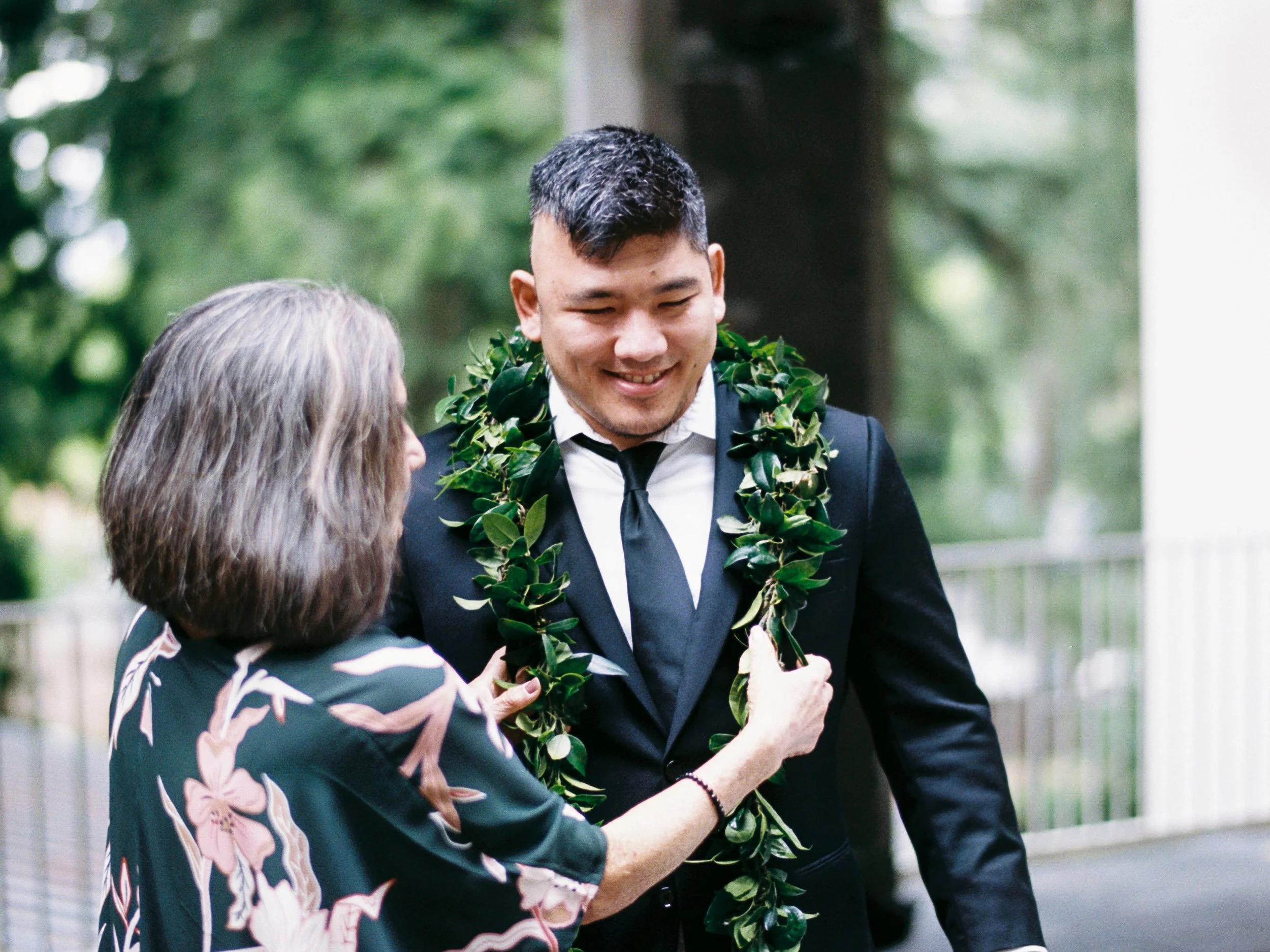 Groom smiles as a woman places a traditional green lei around his shoulders.