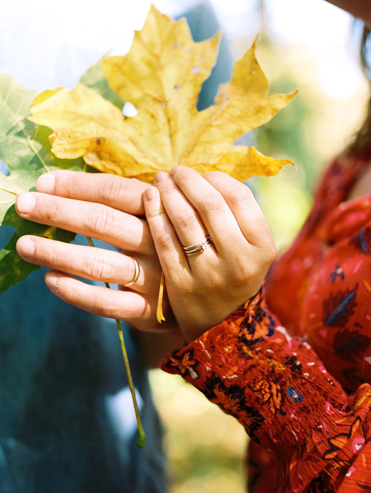 Close-up of hands holding a yellow autumn leaf with engagement rings visible during fall engagement photos Oregon