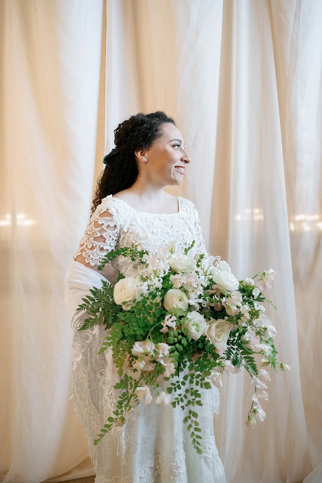 Bride in a vintage white lace gown holding a large cascading bouquet of white flowers and ferns.