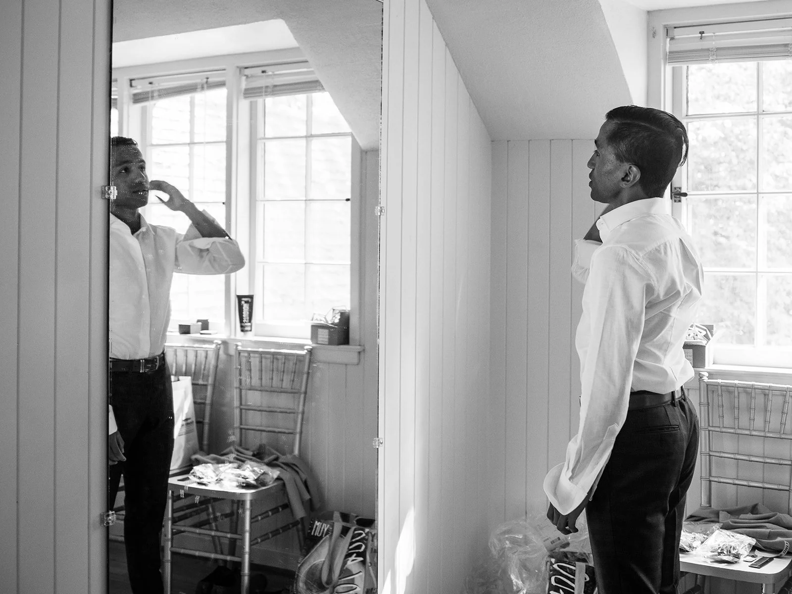 Groom adjusts his shirt collar while looking into a mirror before the wedding.