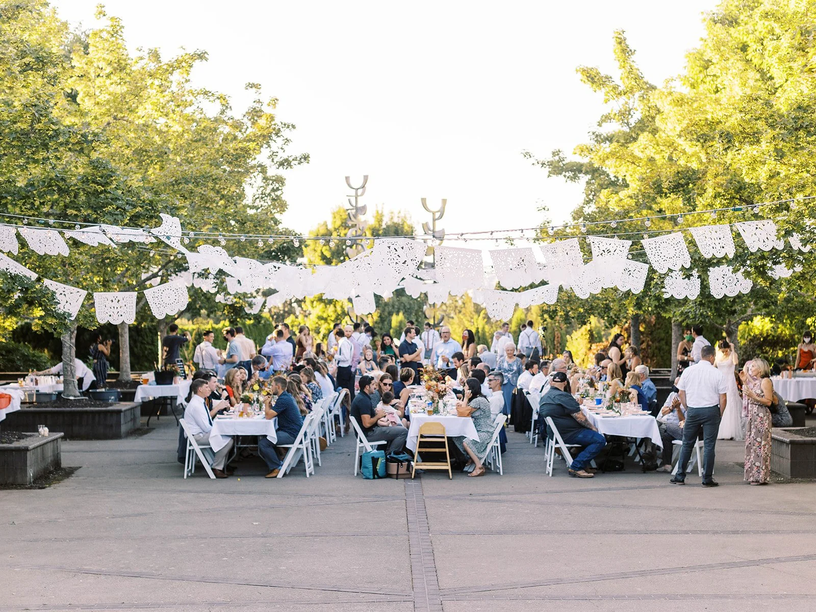 Outdoor wedding reception with guests seated at long tables under hanging banners