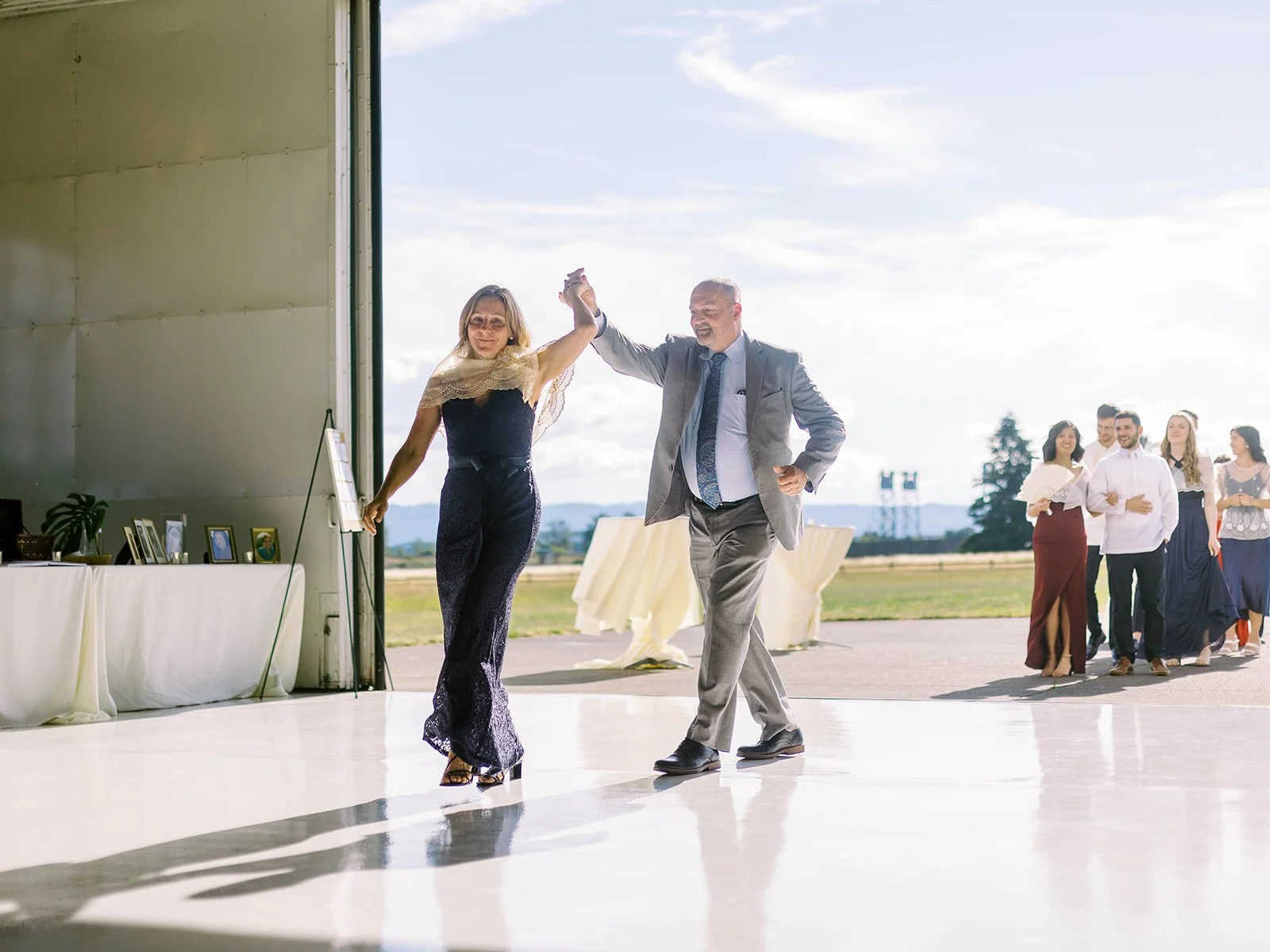 Couple spinning together during their reception entrance into the Pearson Air Museum hangar, with wedding party members following behind on the tarmac