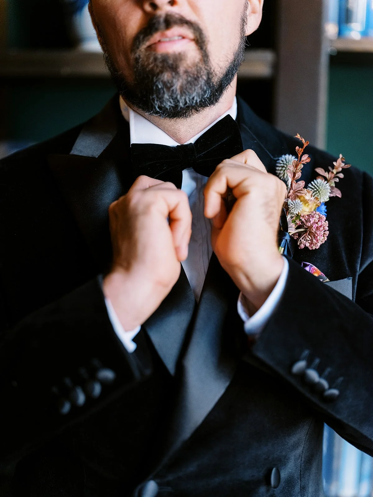 Groom in a black tuxedo adjusting his bow tie with a colorful floral boutonniere at the Sentinel Hotel.