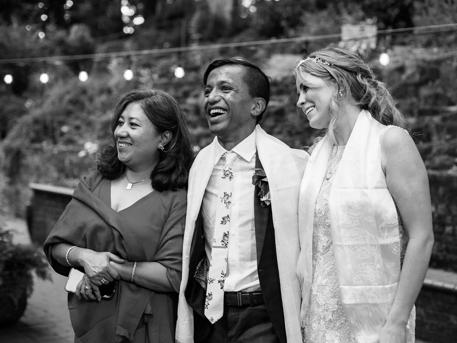 Black-and-white portrait of the newlyweds standing beside a woman after a cultural wedding blessing.