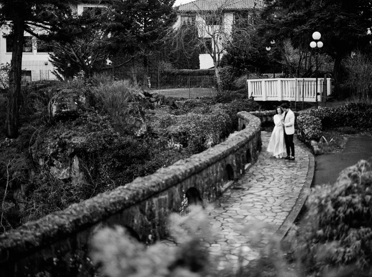 Black and white film photograph of a couple walking along the stone pathways at Columbia Gorge Hotel, surrounded by gardens and old-world architecture.
